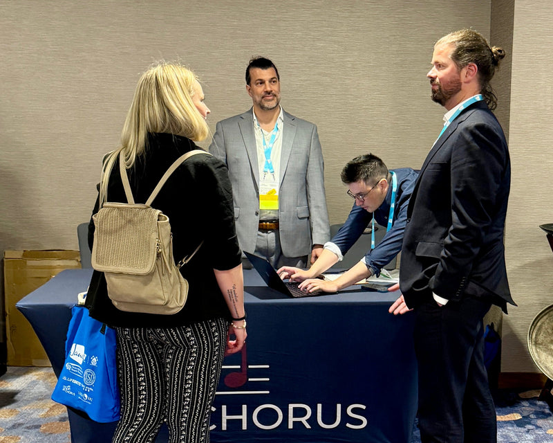People interacting at a cHorus event with a table and branding.