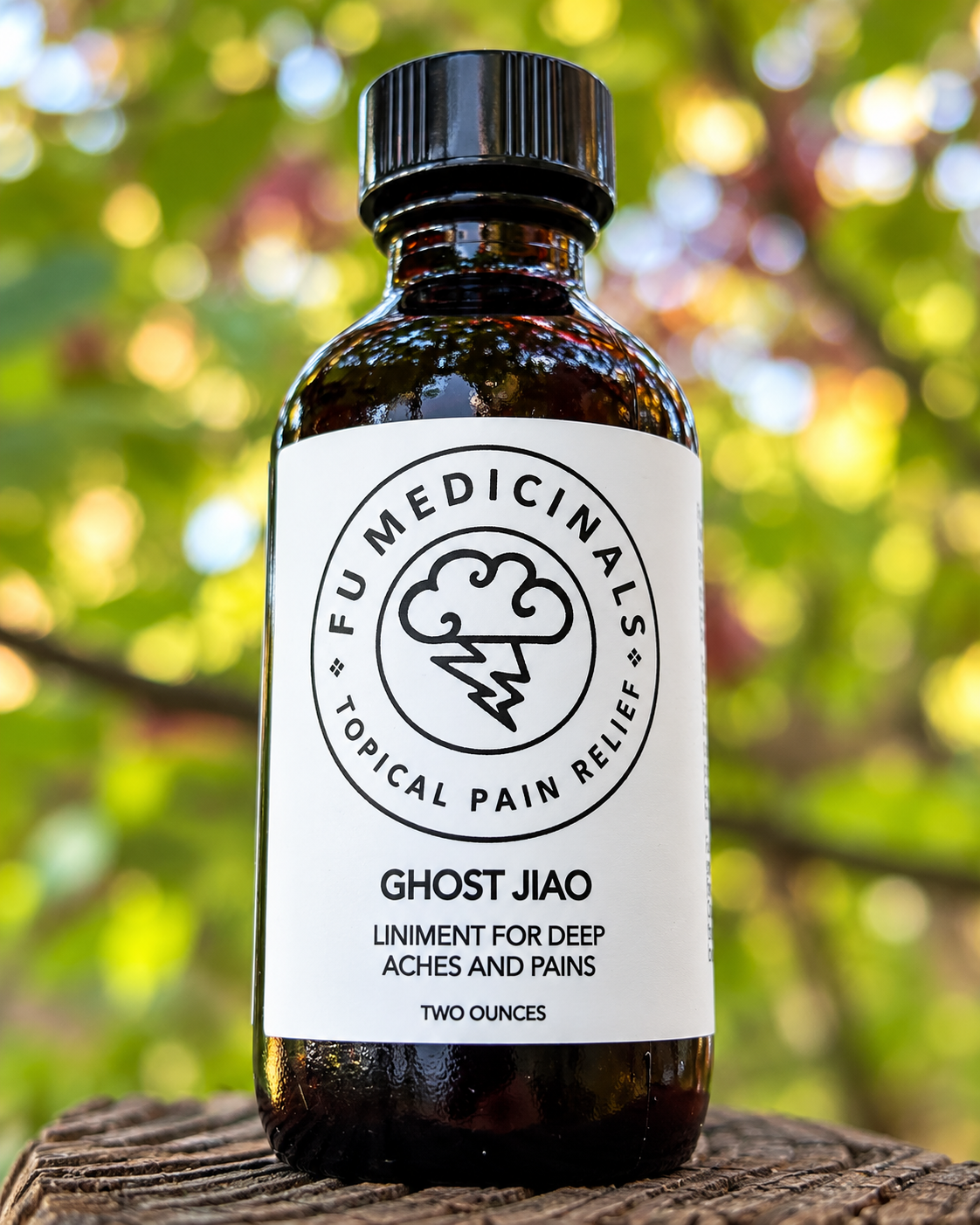 A bottle of Ghost Jiao herbal liniment by Fu Medicinals on a rustic wooden surface with a blurred green outdoor background.
