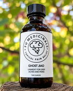 A bottle of Ghost Jiao herbal liniment by Fu Medicinals on a rustic wooden surface with a blurred green outdoor background.